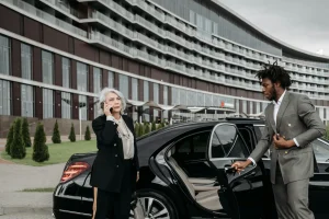 Man in a gray suit opening a black car door in front of a modern building.