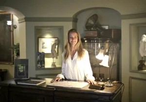 Person in a white shirt standing at an antique desk with a map and vintage items.